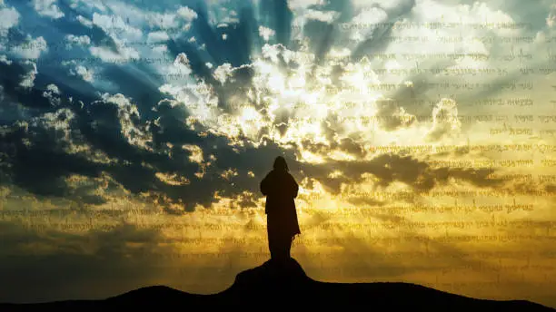 Silhouette of Jesus praying on a hill crest with sun rays. Old scroll