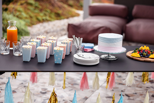 Beautifully set table for a gender reveal party at a rooftop terrace. There are no people since the guests haven't arrived yet. The table is full of delicious sweets and snacks that are waiting for the guests.