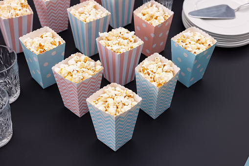 Popcorn snack in  cute pink and blue paper boxes set on a table before a gender reveal party.