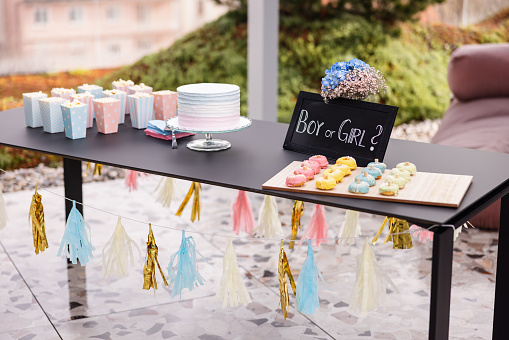 A table on a rooftop terrace decorated with gender reveal decorations. There are some delicious snacks and sweets on the table waiting for the guests. There are no people. Cute baby shower decoration idea.