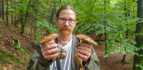 Young men in forest showing two boletus in hand