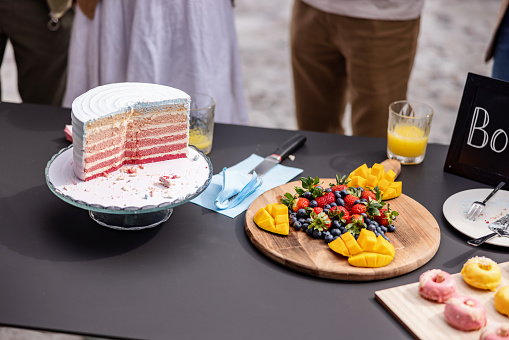 Beautiful and delicious pink cake at a gender reveal party accompanied by other vibrant and fun snacks such as doughnuts and fresh fruit. Since the cake is pink, the expectant couple is having a baby girl. Delicious party food for gender reveal parties and baby showers.