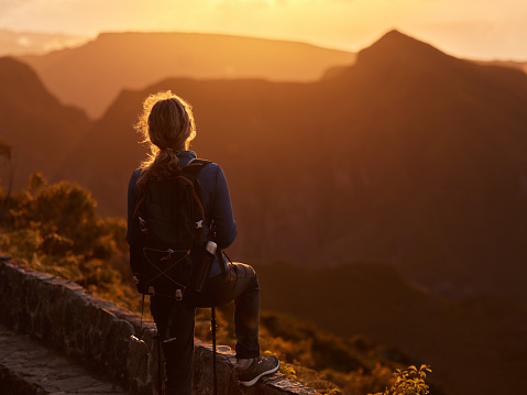 Rear view of a female hiker looking at view while having a break on a mountain at sunset. Copy space.