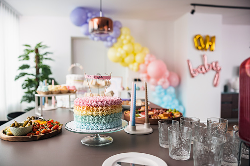 Beautiful baby shower decorations in a modern apartment before the baby shower. The decorations are fun, girly, and colorful. There are some delicious sweets and desserts placed on the dining table.