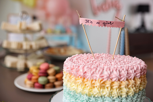 Beautiful colourful cake placed on a dining table before a baby shower celebration. The cake is in pastel colours and surrounded by amazing decorations and delicious party foods. Amazing modern baby shower inspiration.