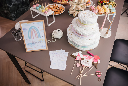 Cute baby shower decorations on a table next to some delicious and colorful snacks/sweets that are waiting for the guests. The table is set beautifully. There are some photo props on the table.