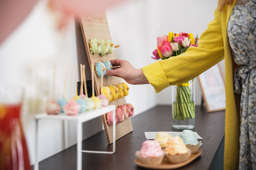 Unrecognizable Caucasian woman taking a colorful doughnut at a baby shower celebration. Delicious desserts and snacks ready for the guests to take.