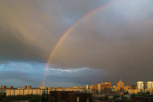 a rainbow after rain on the background of rain clouds over city buildings on a summer day