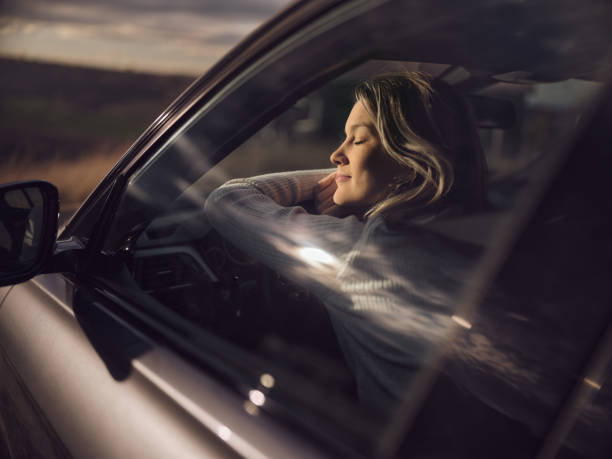 Smiling woman resting with her eyes closed in a car. The view is through glass. Photographed in medium format.