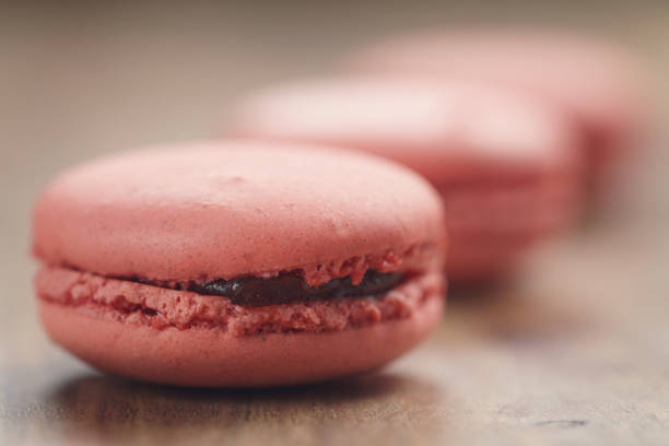 closeup shot pastel colored macarons with strawberry flavour on wood table, vintage toned photo