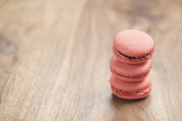 closeup shot stack of pastel colored macarons with strawberry flavour on wood table, vintage toned photo