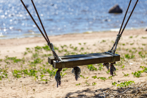 Old wooden swing on the ropes on the summer beach close-up. Swing in focus, background blurred.