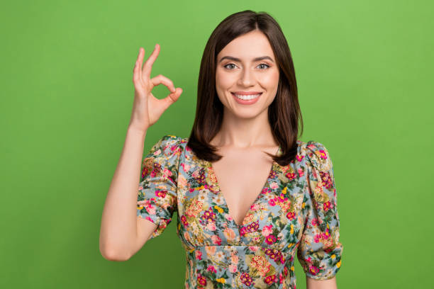 портрет великолепной позитивной леди, сияющей улыбкой, пальцы рук демонстрируют символ окея, изолированный на зеленом фоне - people cleavage color image clothing стоковые фото и изображения