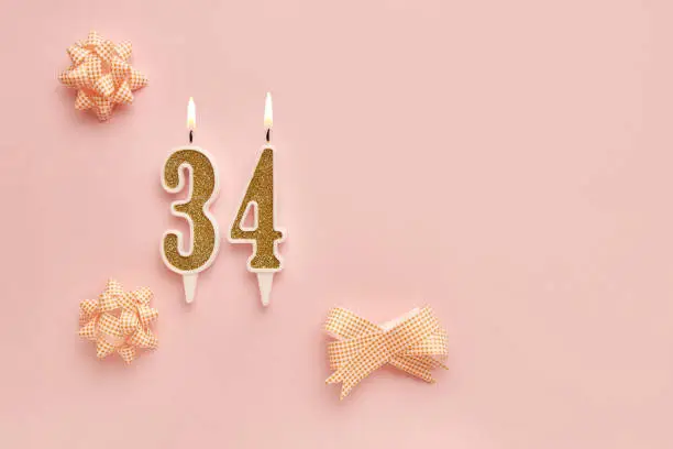 Number 34 on a pastel pink background with festive decorations. Happy birthday candles. The concept of celebrating a birthday, anniversary, important date, holiday. Copy space. banner