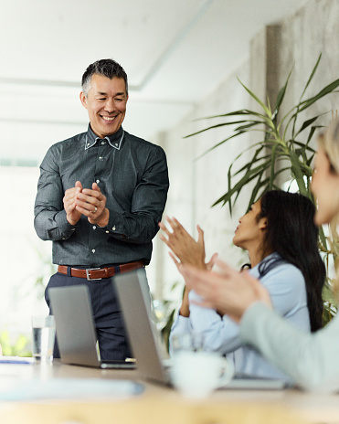 Happy Chinese manager and his colleagues applauding after successful meeting in the office.