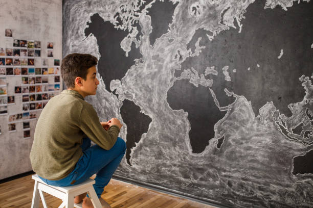 ragazzo adolescente che si siede davanti alla pittura della mappa del mondo - paintings child house childhood foto e immagini stock