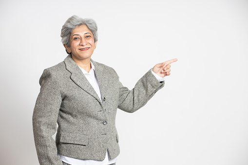 Smiling confident mature senior indian woman point finger at blank space for advertisement or promotion. Asian Middle aged businesswoman,60s gray-haired lady executive business leader manager.