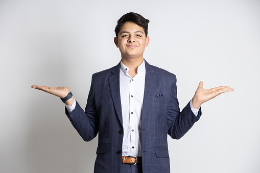 Portrait of happy young Indian teenager boy wearing suit with his arms and hands raised isolated on white studio background, copy space for advertisement and promotion.
