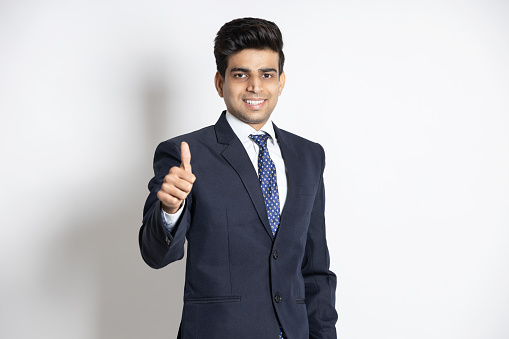 Portrait of a happy confident young indian teenager boy wearing suit do thumbs up isolated on white background.
