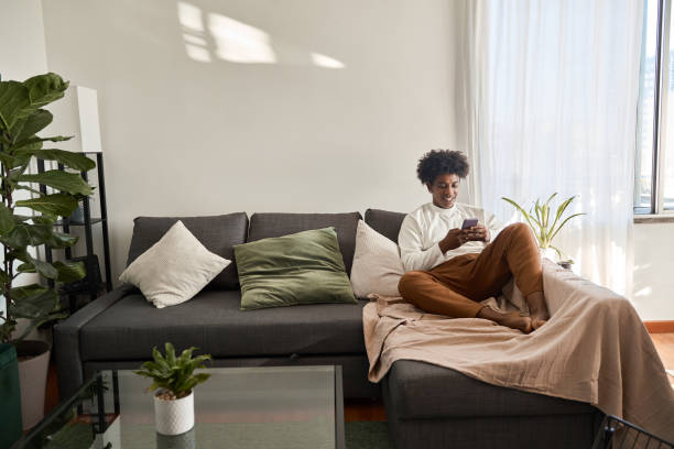Relaxed cool gen z African American teen sitting on couch using phone.