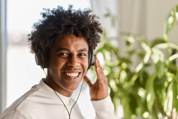 Happy gen z African American guy wearing headphones listening music at home.