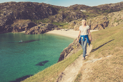 Woman walking on the high path linking the two beaches at Achmelvich near the village of Lochinver on the north west coast of Scotland. Part of the North Coast 500 road trip.