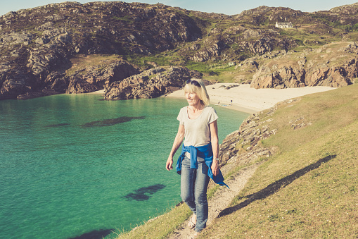 Woman walking on the high path linking the two beaches at Achmelvich near the village of Lochinver on the north west coast of Scotland. Part of the North Coast 500 road trip.