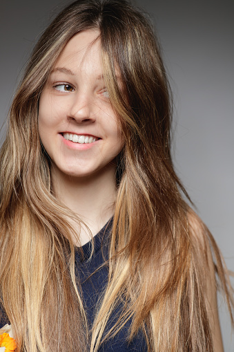 Portrait of beautiful teenage girl with long naturally blond hair looking away with cheerful smile, studio shot