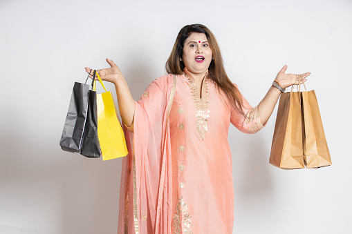 Surprised overweight indian woman holding shopping bags. fat asian female shopper wearing ethnic outfit, isolated over white studio background, black Friday deal, discount. festival diwali sale