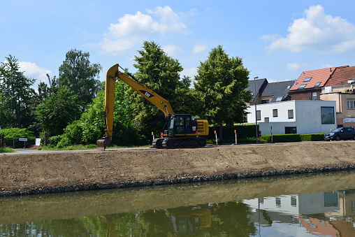 Wijgmaal, Vlaams-Brabant, Belgium - June 23, 2023: canal bank is excavated by a bulldozer and reinforced with boulders in a cage