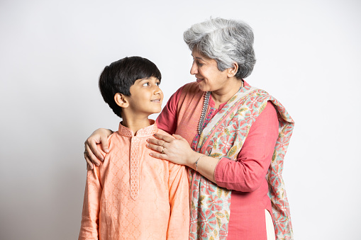 Happy young indian grandmother with her little grandson wearing ethnic festive outfit isolated over white background. Smiling asian family. Senior woman with little child boy looking at each other..
