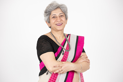 Happy senior indian woman wearing saree standing cross arms isolated over white background, Confident Asian elderly female looking at camera with folded hands. closeup.