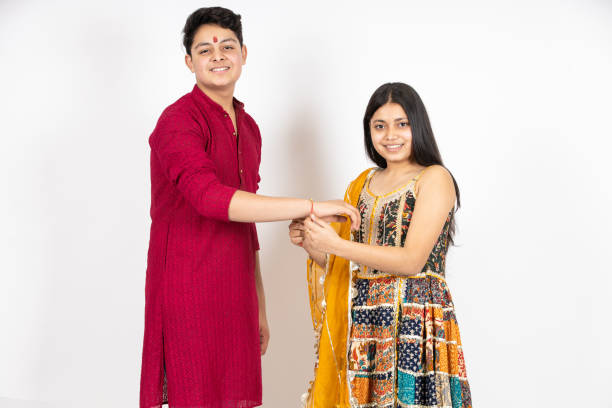 Portrait of happy indian teenage girl tying rakhi on young brother's hand occasion of rakshabandha or bhi dooj isolated on white studio background. both wearing traditional festive cloths. Portrait of happy indian teenage girl tying rakhi on young brother's hand occasion of rakshabandha or bhi dooj isolated on white studio background. both wearing traditional festive cloths. raksha bandhan stock pictures, royalty-free photos & images