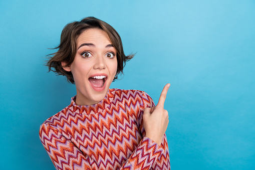 Photo of excited funky woman dressed striped top open mouth pointing empty space isolated blue color background.