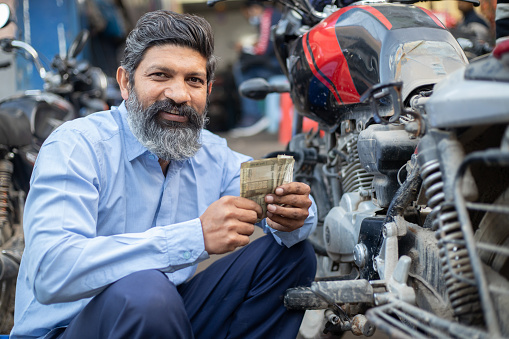 Happy Professional Indian mechanic counting money in motorcycle repair shop.
