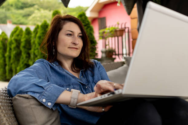 istock Woman using laptop while relaxing at backyard. She has online meeting. Web chat, connection, communication online, business, work from home, distance studying, learning, technology concept 1500839662