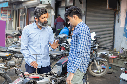 Professional Indian mechanic repairs motorcycle with screwdriver. Asian man repairing motorbike in repair shop.