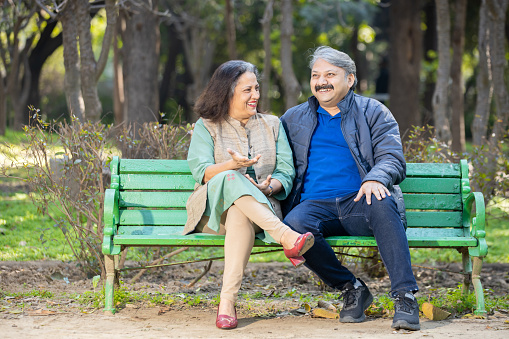 Happy Indian or asian senior couple talking laughing while sitting on the bench, Old man and woman relaxing at park spend time together, relationship and people concept.