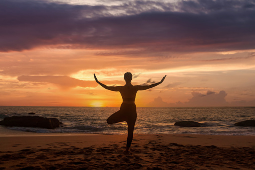 Silhouette slim woman does yoga position arms raised on tropical sea coast or ocean beach outdoors at sunset. Female performs exercises for healthy lifestyle to restore strength and spirit. Copy space
