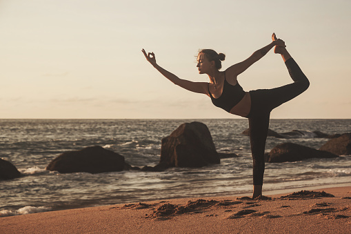 Young woman does yoga for healthy lifestyle on sea beach. Female performing sports exercises to restore strength and spirit. Yoga position on seashore