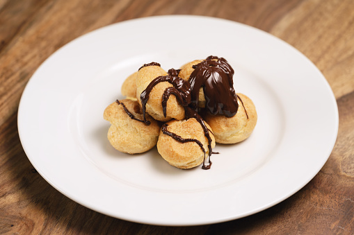 profiteroles covered with black chocolate on plate closeup, shallow focus