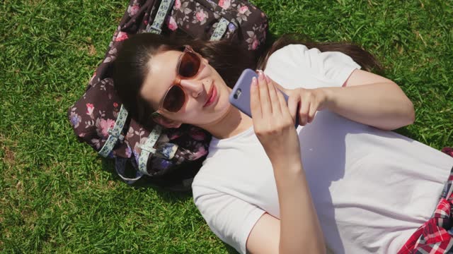 Top view of happy young woman lying outdoors in park using mobile phone