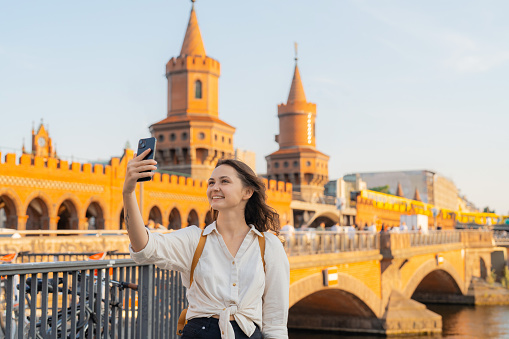 Woman in white shirt using smartphone while walking in Berlin on the background of Oberbaumbrucke