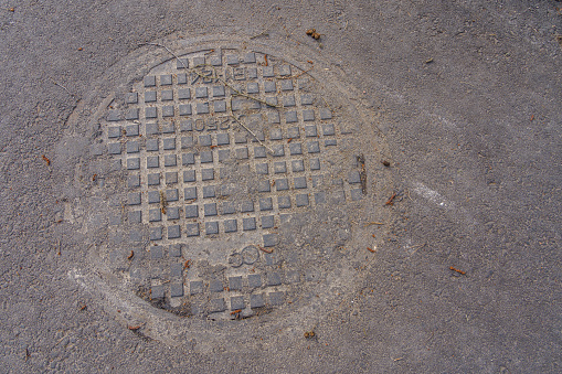 Manhole cover on asphalt, covered with pollen and dust, top view