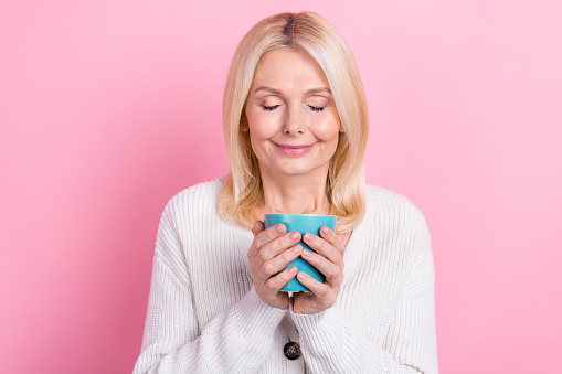 Portrait of cheerful person with blond hairstyle dressed white sweater hold cup smell unsurpassed taste isolated on pink color background.