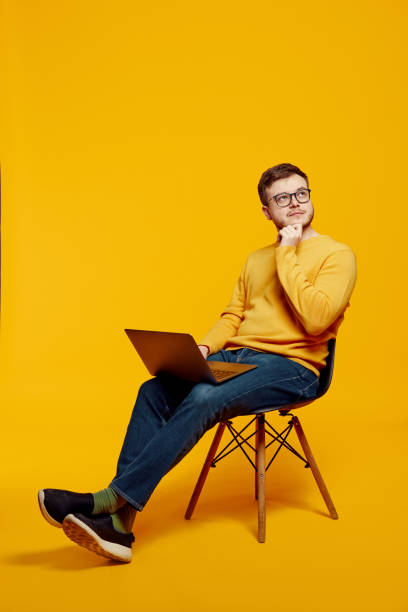istock Thoughtful man holding laptop computer and touching chin with hand while sitting on chair 1500848469