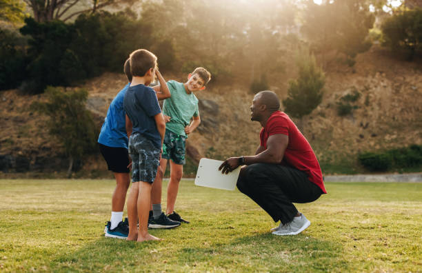 coach having a team talk with children in a school ground - soccer child coach childhood imagens e fotografias de stock