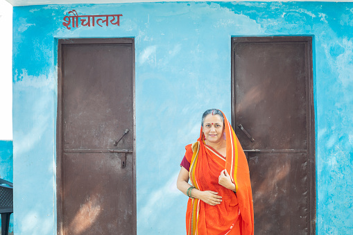 Portrait of of happy senior indian woman standing outside public toilet solves the problem for many females in india.