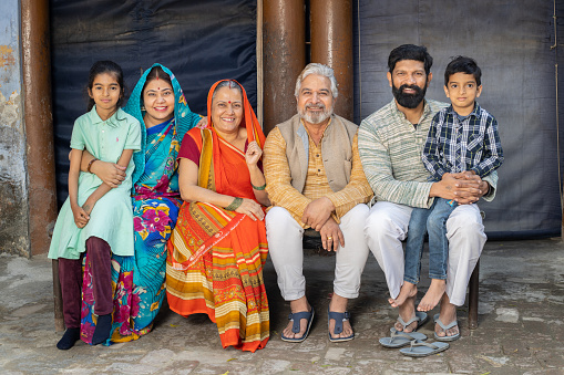 Portrait of happy rural indian joint family sitting together looking at camera.