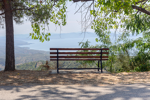 Panoramic view of the sea, mountains in the distance and a bench in the shade under the trees on a sunny summer day (Greece, Thessaly, Pelion)